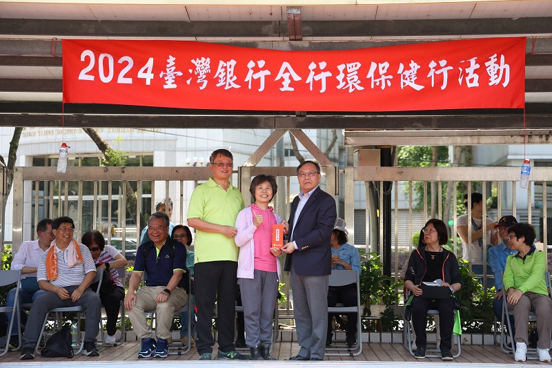 臺灣銀行舉辦2024全行環保健行活動摸彩，該行董事長呂桔誠(右)、職工福利委員會主委陳俊雄(左)與得獎者開心合影。